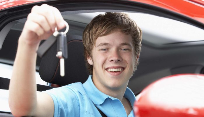 Teenage boy holding car keys sitting in car