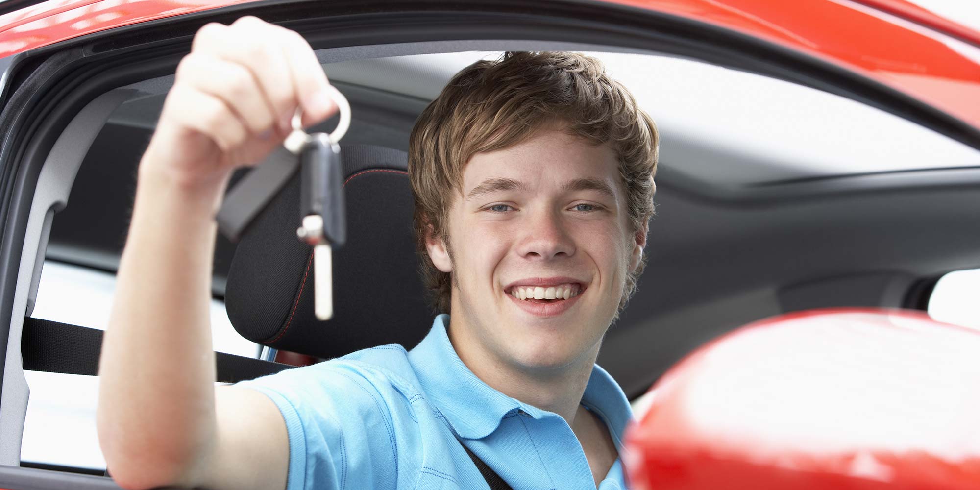 Teenage boy holding car keys sitting in car